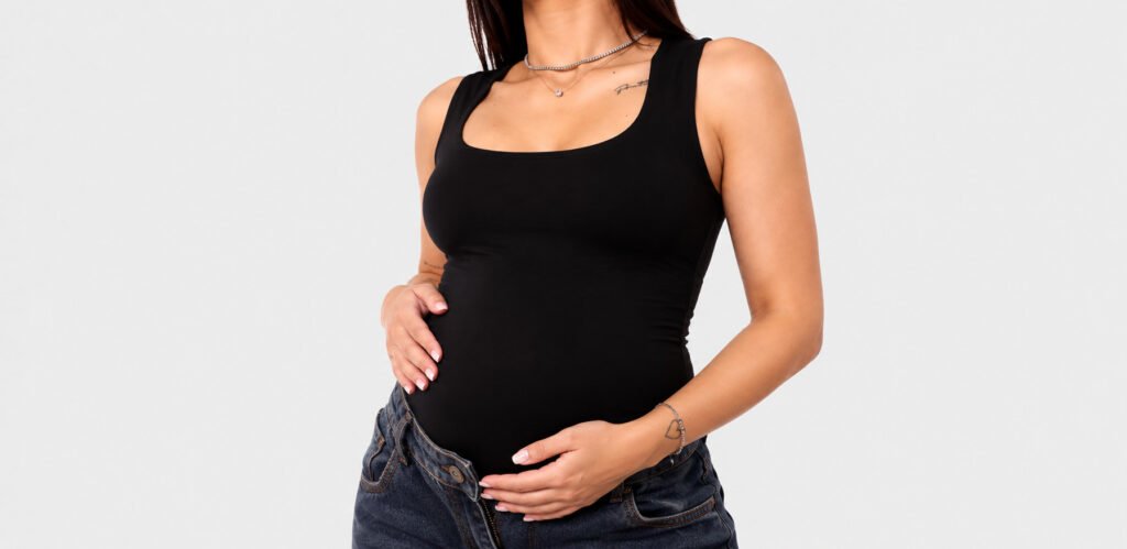 Mulher grávida usando body preto justo com jeans escuro